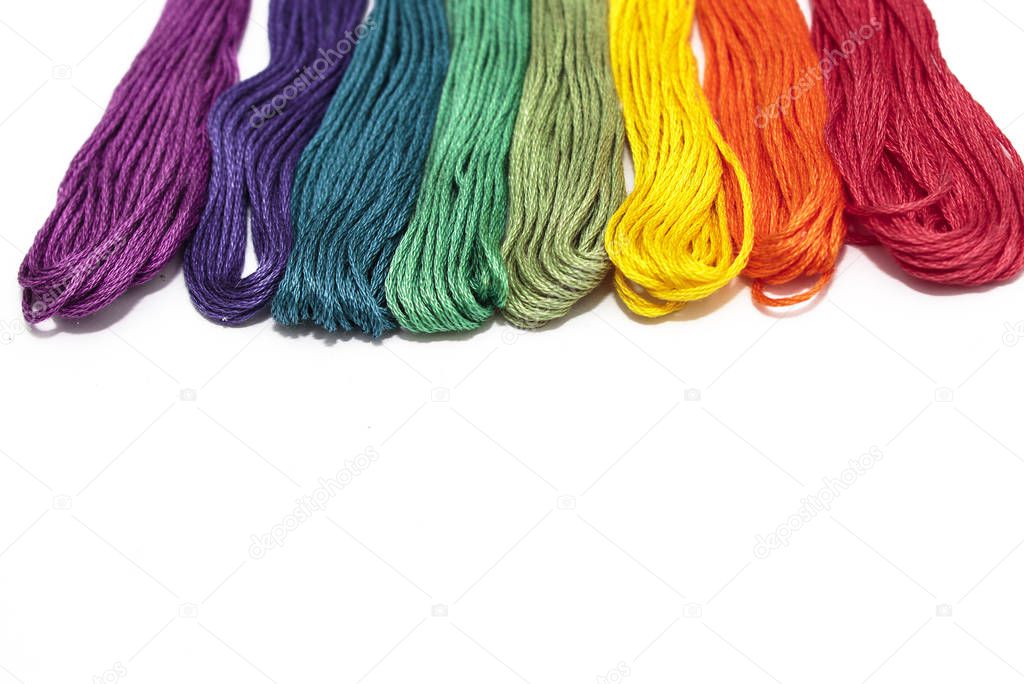 Colored threads for embroidery, seven colors of the rainbow lie in a row on a white background