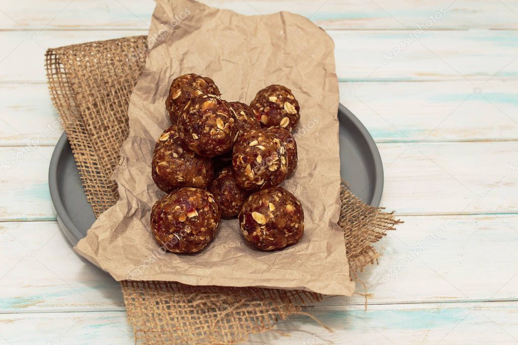 Homemade energy balls like a healthy breakfast or a snack of raisins, dried apricots, dates, nuts and oatmeal. Energy balls lie on crumpled paper on a gray ceramic plate on a white background. Horizontal orientation.
