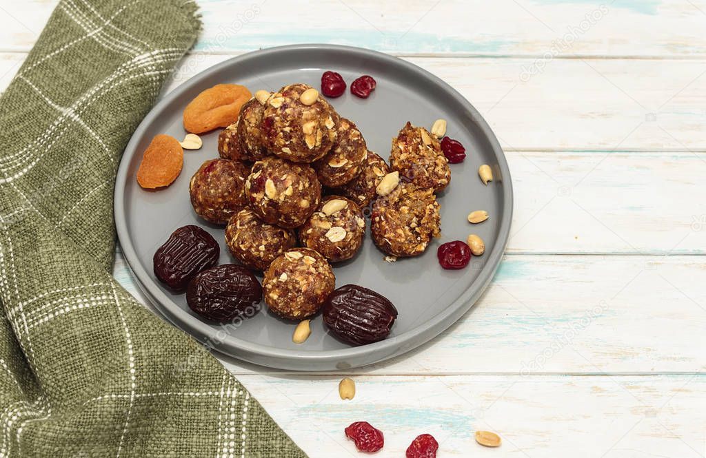 Homemade energy balls like a healthy breakfast or a snack of raisins, dried apricots, dates, nuts and oatmeal, that lie on  a gray ceramic plate on a white wood background and green towel. Horizontal orientation.
