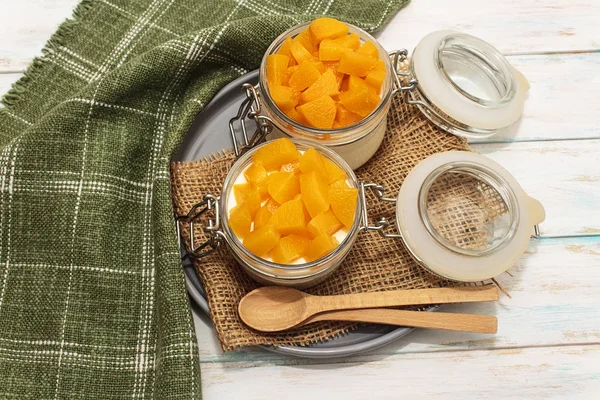 Panna cotta classical italian desert with peaches in white jar on a blue wooden background on a gray plate and two wodden spoons, green towel