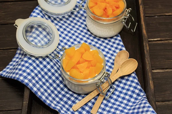 Panna cotta classical italian desert with peaches in two white jar on a brown wooden background on blue towel with two spoons