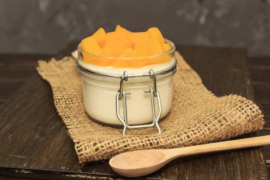 Panna cotta klasik İtalyan çölü, şeftalili beyaz bir kavanozda kahverengi ahşap bir arka planda bir kaşık bez.