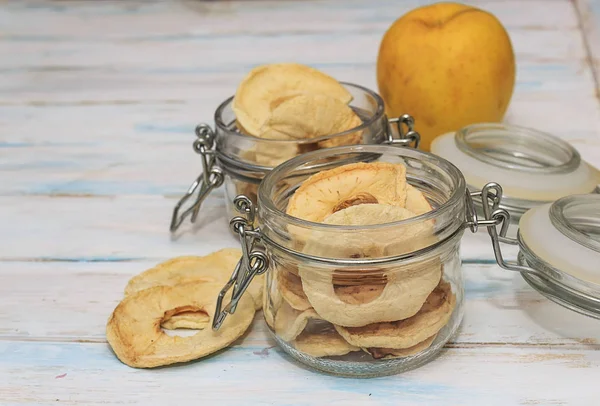 Dried apple chips in a glass jar and yellow apple on a white wooden background. Diet snack with copy space.