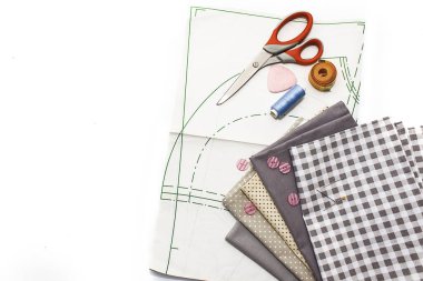 Tools for sewing on a white background. A set of fabrics, a pattern, threads, buttons, scissors. Flat lay, copy space.