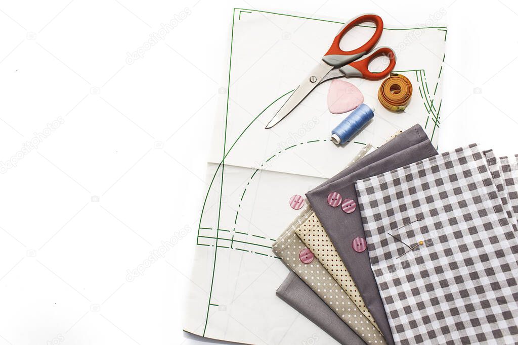 Tools for sewing on a white background. A set of fabrics, a pattern, threads, buttons, scissors. Flat lay, copy space.