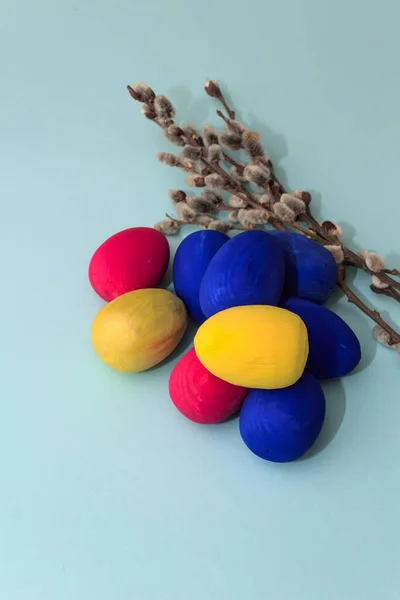 Modern easter colored eggs and willow branches on a blue background. Easter decorative composition with copy space.