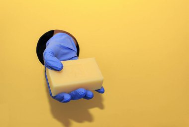 Womens hand in a blue gloves hold a soap on a yellow background. Hand hygiene and protection during the coronavirus epidemic clipart