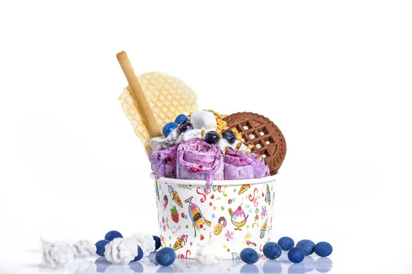 rolls of ice cream with cookies and colorful decoration in a paper cup against a white background