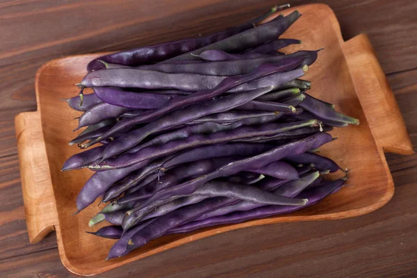 Purple string beans on a wooden plate on a wooden background — Stock Photo, Image