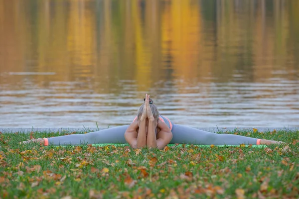 Młoda kobieta robi joga w parku miejskim jesień, w pobliżu rzeki — Zdjęcie stockowe