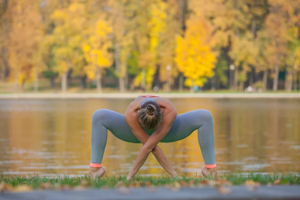 Młoda kobieta robi joga w parku miejskim jesień, w pobliżu rzeki — Zdjęcie stockowe