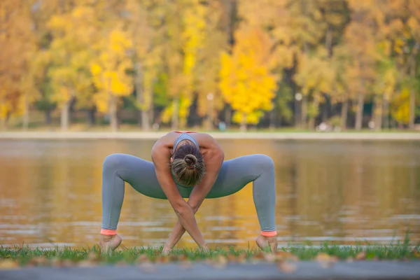 Ung kvinde gør yoga i efteråret bypark nær floden - Stock-foto