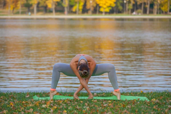 Giovane donna che fa yoga nel parco della città di autunno vicino al fiume — Foto Stock