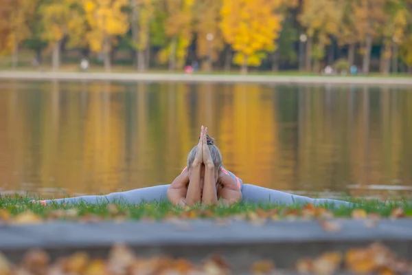 Ung kvinna gör yoga i höst stadsparken nära floden Stockfoto