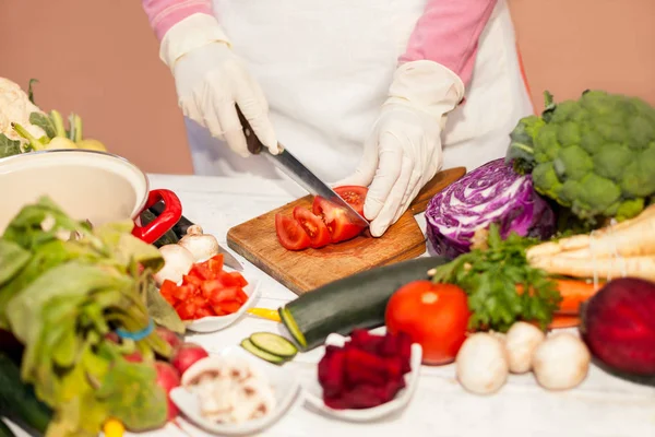 Frau mit Handschuhen schneidet Tomate auf Schneidebrett — Stockfoto