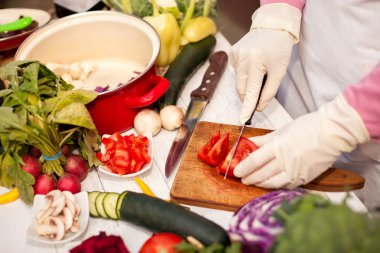 Kadın eldivenler ile domates parçalar üzerinde bir bıçak ile kesmek