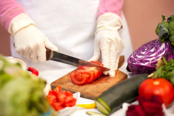 Vrouw met handschoen snijden tomaat in de keuken — Stockfoto