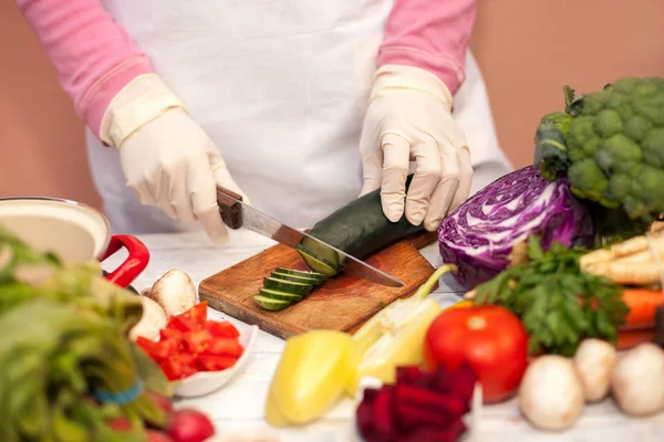 Vrouw met witte handschoen snijden komkommer in de keuken — Stockfoto