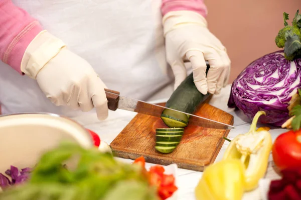 Frau mit weißen Handschuhen schneidet Gurke in der Küche — Stockfoto
