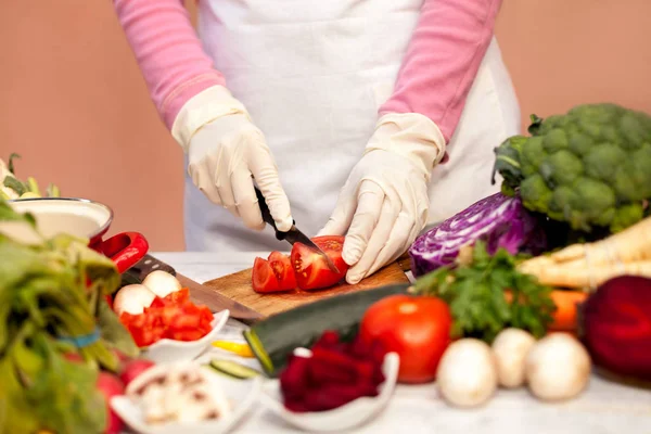 Vrouw met witte handschoen snijden tomaat in de keuken — Stockfoto
