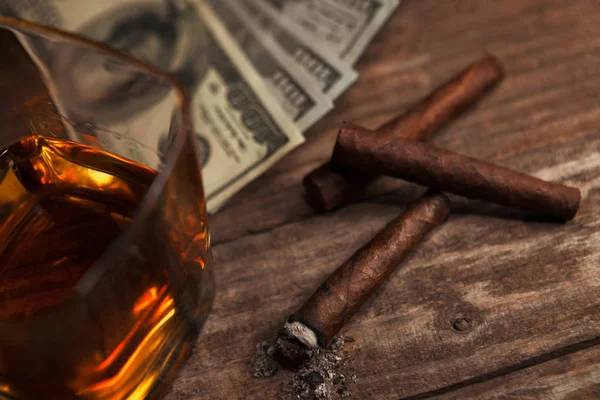 Cigarrillos, vidrio con brandy y dinero en el fondo — Foto de Stock