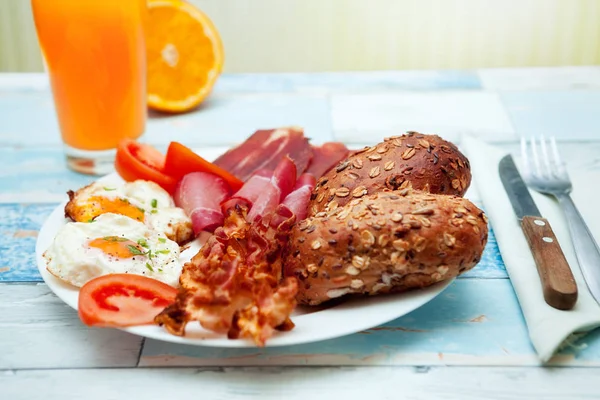 Delicioso café da manhã com ovos fritos, pães, bacon e presunto em um pl — Fotografia de Stock