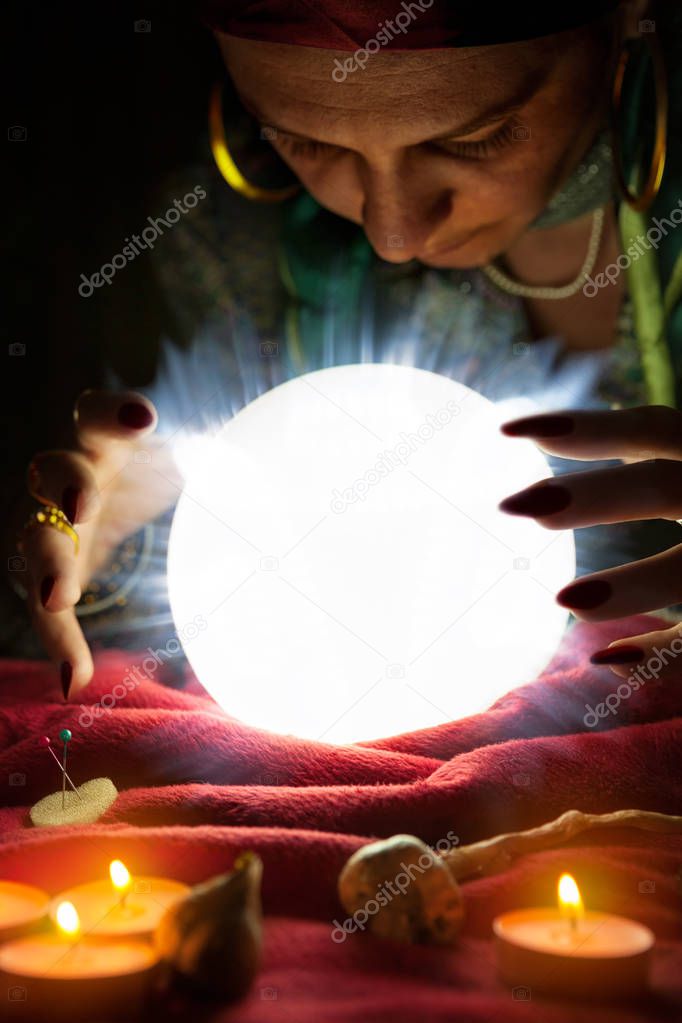 Gypsy fortune teller staring in crystal ball with her hand above crystal ball