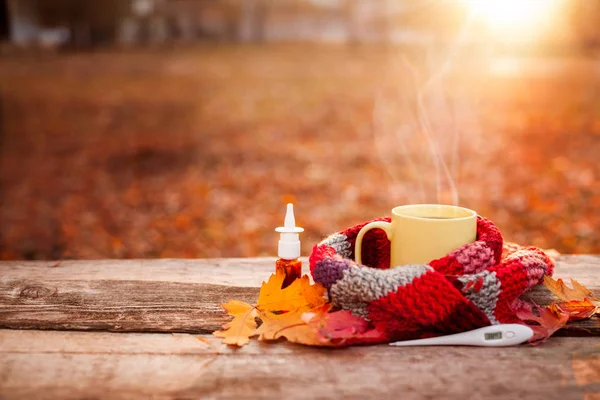 Teetasse bedeckt mit warmem Schal, Nasentropfen und Thermometer auf dem Tisch — Stockfoto