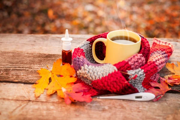 Taza de té con bufanda caliente, termómetro y gotas para la nariz en su madera — Foto de Stock