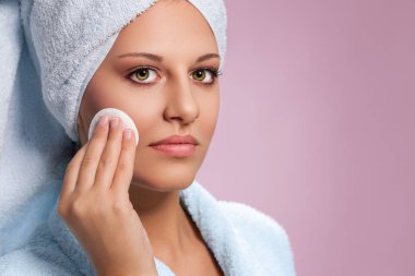 Pamuklu bezle yüzünü temizleyen genç bir kadın.