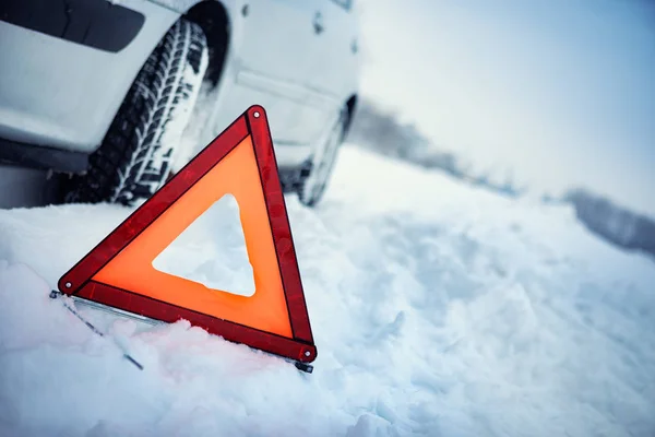 Fechar o triângulo de aviso vermelho com um carro avariado em winte — Fotografia de Stock