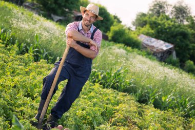 Yakışıklı genç adam elinde çiftçilik aleti tutuyor.