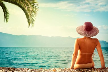 Plaj kadını, güneşin altında dinlenip, tropikal kaçış cennetinde mükemmel turkuaz okyanusu seyrederek lüks tatilin tadını çıkarıyor. Arkada güneşlenen kız..