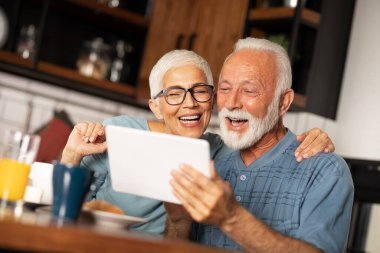 Mutfakta dijital tablet taşıyan gülümseyen yaşlı çiftin portresi.