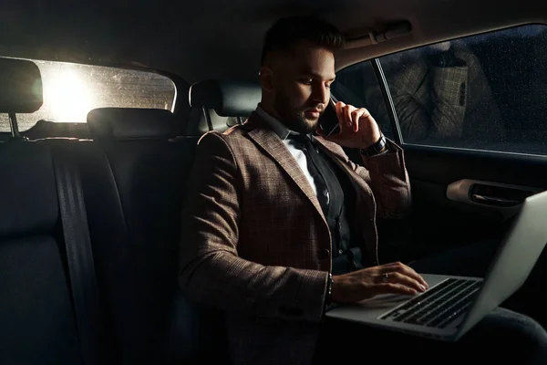 guy in car with laptop and phone