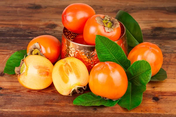 Persimmons with vintage copper vase on old wood — Stock Photo, Image