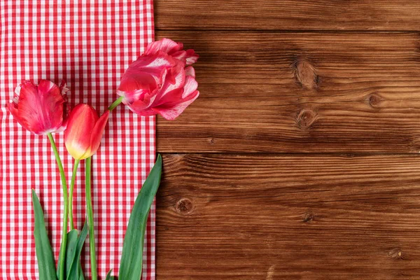 Tulipány s červeně kostkovaný ubrus na zemi dřevěné pozadí. Pohled shora, text prostoru — Stock fotografie