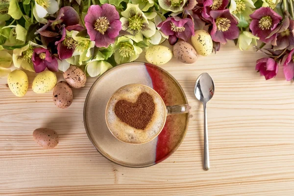 Coffee with heart shape and flowers Easter decoration on wooden table. Top view