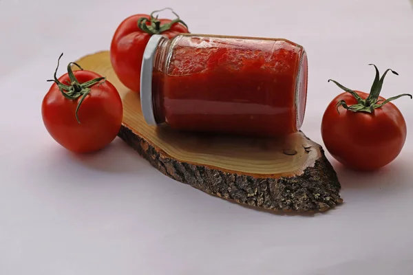 Tomato paste in jar and tomatoes on white background.