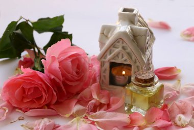 Beyaz arka planda pembe güller ve şişede gül yağı..