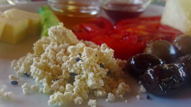 Beyaz tabakta kahvaltı, domates, peynir, bal, reçel, zeytin, salatalık.