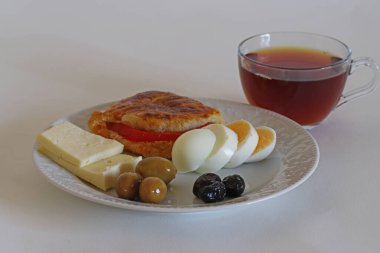 Poacha, peynir, yumurta, zeytin, domates ve çay beyaz bir tabakta.