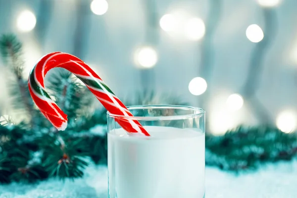 Christmas milk glass with candy, decorations, snow, christmas tree branches on bokeh blurred light New Year background. Free space