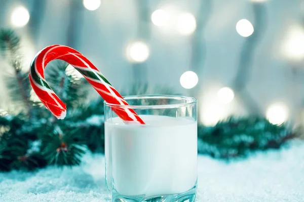 Christmas milk glass with candy, decorations, snow, christmas tree branches on bokeh blurred light New Year background. Free space