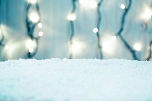 Christmas background with bokeh of a luminous garland and snow on wooden table