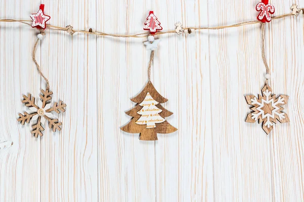 Os brinquedos de madeira de Natal na forma de uma árvore de Natal e flocos de neve pesam em uma corda em um contexto de madeira branco. Belo cartão festivo com espaço livre — Fotografia de Stock