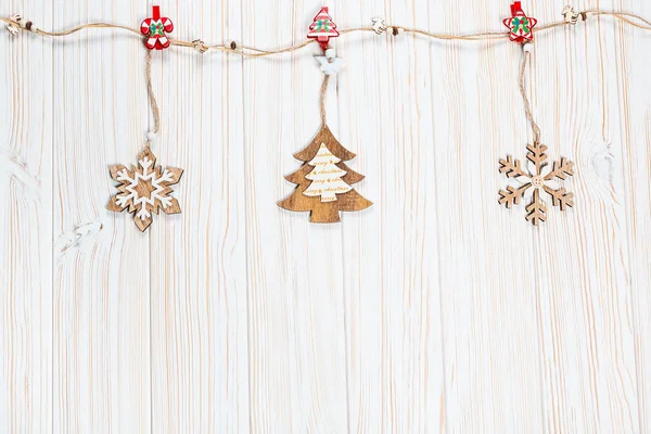 Beyaz ahşap zemin üzerinde bir ip üzerinde bir Noel ağacı ve kar taneleri şeklinde ahşap oyuncaklar Noel tartın. Güzel bayram tebrik kartı boş alan ile
