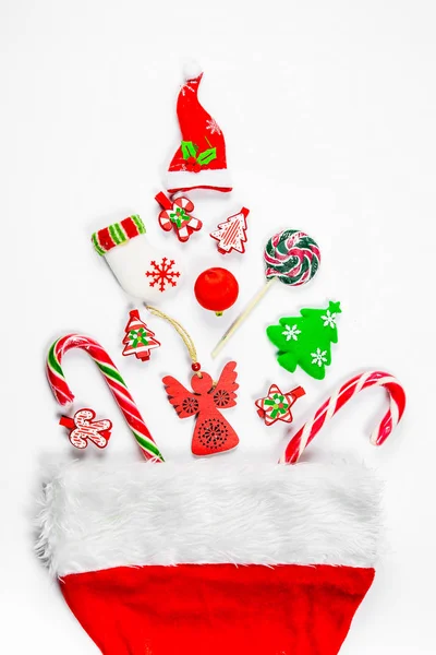 Kerstmis achtergrond met een kerstmuts waaruit verspreid geschenken, snoep, Nieuwjaars versieringen speelgoed op een witte achtergrond. Concept van reclame, winkelen, kortingen en geschenken voor de wintervakantie — Stockfoto