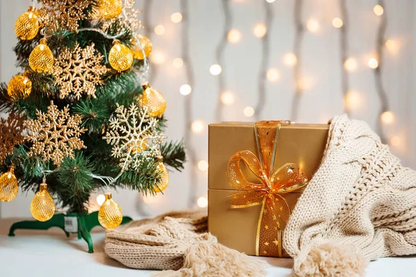 Un árbol de Navidad decorado copos de nieve y una guirnalda, regalo con bufanda de punto en el fondo de un bokeh y tablas blancas. Feliz Navidad, ideas para postales para vacaciones de invierno — Foto de Stock