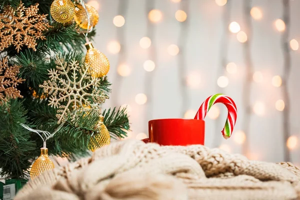 Un sapin de Noël décorait des flocons de neige et une guirlande, une tasse de café, des bonbons avec une écharpe tricotée sur le fond d'un bokeh et des planches blanches. Joyeux Noël, idées de cartes postales pour les vacances d'hiver — Photo